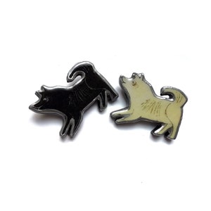 May include: Two enamel pins featuring black and white stylized illustrations of dogs. The black dog is facing left and the white dog is facing right.