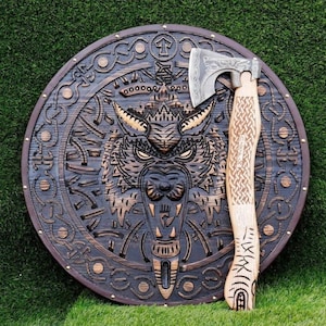 May include: A wooden shield with a carved wolf design and an axe. The shield is round, dark brown, and features intricate carvings. The axe has a light-colored wooden handle with etched patterns and a silver-colored head.