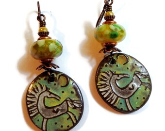 May include: A pair of green and brown ceramic earrings with a stylized horse design. The earrings feature a green and yellow glass bead with copper accents.
