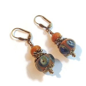 May include: A pair of dangle earrings with orange and blue glass beads. The beads have a gold-toned metal accent with a floral design. The earrings have a gold-toned hook closure.