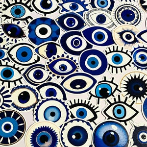 May include: A collection of blue and white evil eye stickers in various shapes and sizes. The stickers feature a central blue eye with white and black details, surrounded by different designs, including eyelashes and decorative borders. The stickers are arranged on a light pink background.