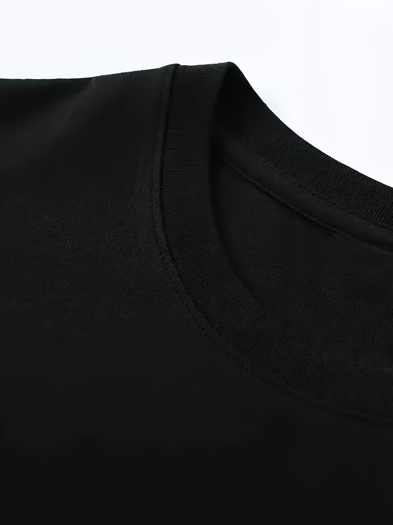 Puede incluir: Primer plano de una camiseta negra con cuello redondo. La tela parece suave y lisa, con un cuello y una costura del hombro visibles. La imagen est&aacute; bien iluminada, destacando la textura y el color de la prenda.