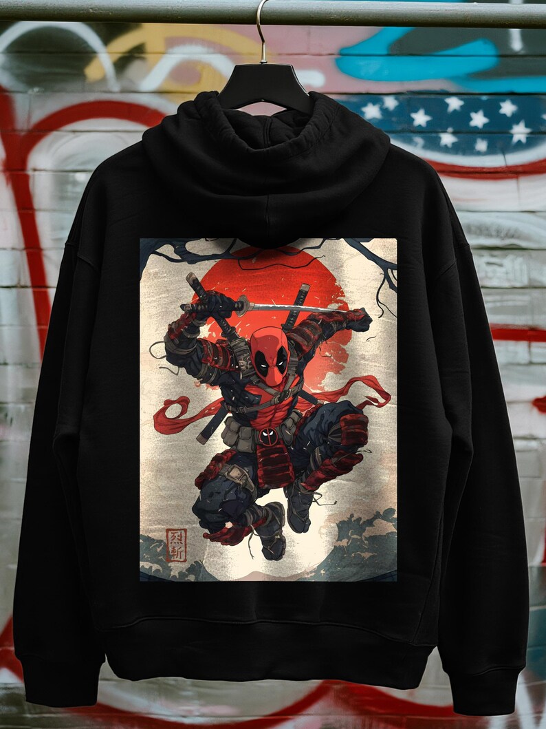 May include: Black hoodie featuring a vibrant graphic of Deadpool in a samurai-inspired pose, set against a red sun and traditional Japanese art elements. The design includes swords and a dynamic action stance.