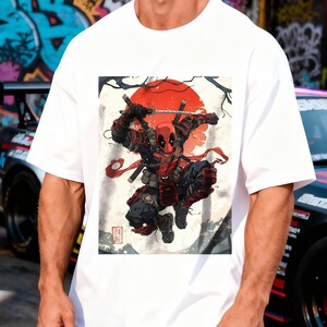 Puede incluir: Camiseta blanca con un gr&aacute;fico de Deadpool empu&ntilde;ando espadas, sobre un sol rojo y un fondo de inspiraci&oacute;n japonesa. El personaje lleva un traje rojo y negro. La camiseta tiene un corte holgado y oversize.