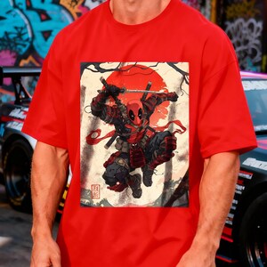 Puede incluir: Camiseta roja con un dise&ntilde;o de Deadpool en una pose de samur&aacute;i, con un sol rojo de fondo. El dise&ntilde;o incluye espadas y texto japon&eacute;s. La camiseta es de color rojo liso.