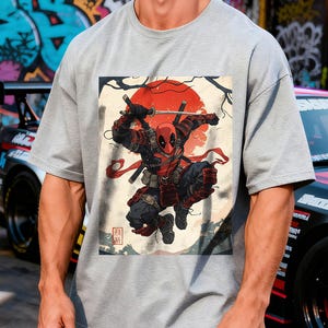 Puede incluir: Camiseta gris con un gr&aacute;fico de un personaje con un traje rojo y negro con una katana, sobre un sol rojo y arte japon&eacute;s. El personaje est&aacute; en una pose din&aacute;mica, con texto japon&eacute;s en la esquina.