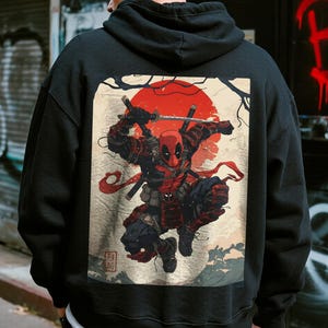 May include: Black hoodie featuring a graphic of Deadpool in a samurai-inspired design. The artwork includes a red sun, swords, and Japanese-style elements. The hoodie is made of a soft material and has a hood and a front pocket.
