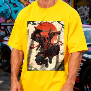 Puede incluir: Camiseta amarilla brillante con un dise&ntilde;o de Deadpool en pose de samur&aacute;i, sobre un fondo beige con un sol rojo y texto japon&eacute;s. La camiseta es de color amarillo brillante.