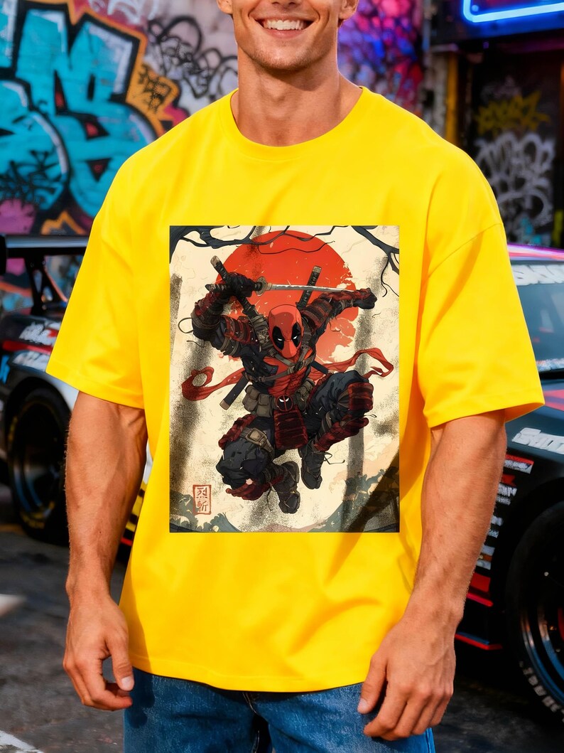 Puede incluir: Camiseta amarilla brillante con un dise&ntilde;o de Deadpool en pose de samur&aacute;i, sobre un fondo beige con un sol rojo y texto japon&eacute;s. La camiseta es de color amarillo brillante.