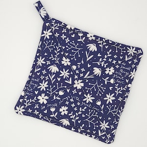 May include: A navy blue square potholder with a white floral pattern and the text "do small things with great love." The potholder has a small loop for hanging.