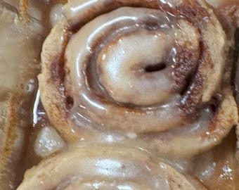 May include: Three cinnamon rolls with a thick layer of white icing. The rolls are in a silver foil container.