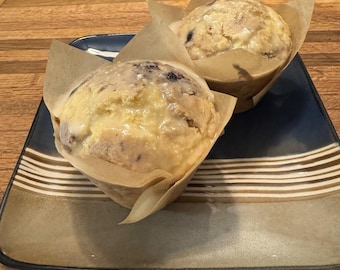 Può includere: Due muffin ai mirtilli con una glassa bianca in cima, su un piatto a strisce blu e marrone. I muffin sono in pirottini di carta.