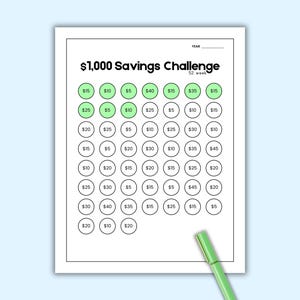May include: A white paper titled "$1,000 Savings Challenge" with a 52-week format. The chart has circles with dollar amounts, some highlighted in green. A green pen rests on the bottom right corner. The background is light blue.