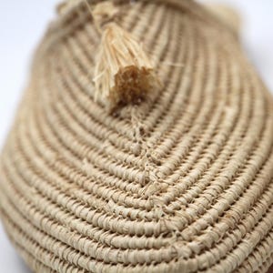 K&ouml;nnte beinhalten: Nahaufnahme eines geflochtenen Strohslippes mit einem kleinen Quasten. Der Slipper ist beige und hat ein nat&uuml;rliches, rustikales Aussehen.