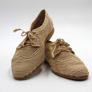 May include: A pair of beige crocheted shoes with lace-up fastenings. The shoes have a woven texture and a casual style.