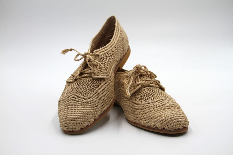 May include: A pair of beige crocheted shoes with lace-up fastenings. The shoes have a woven texture and a casual style.