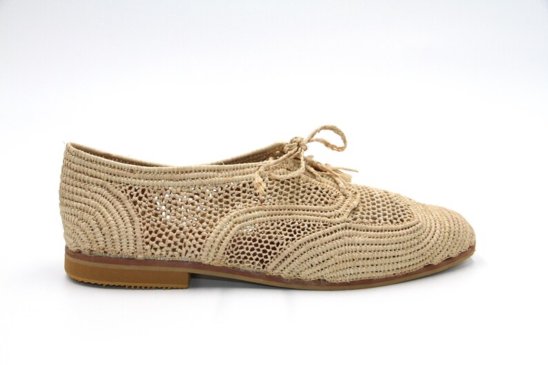 May include: Beige woven crochet flat shoes with a lace-up design.