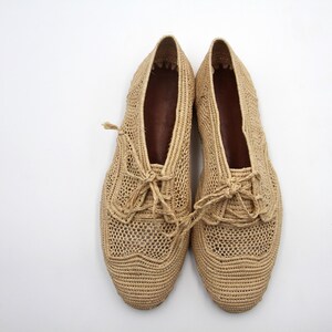 May include: A pair of beige crocheted shoes with lace-up fastenings. The shoes feature a delicate, open-weave design.