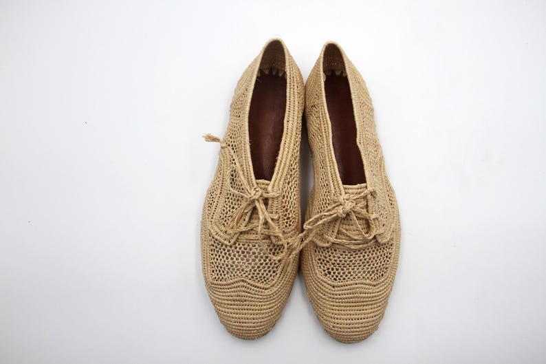 May include: A pair of beige crocheted shoes with lace-up fastenings. The shoes feature a delicate, open-weave design.