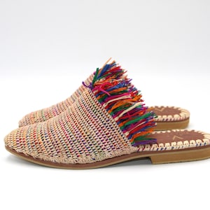 Könnte beinhalten: Ein Paar gewebte beige Sandalen mit einem bunten Fransen-Detail. Die Sandalen haben eine flache Sohle und ein gewebtes Obermaterial.