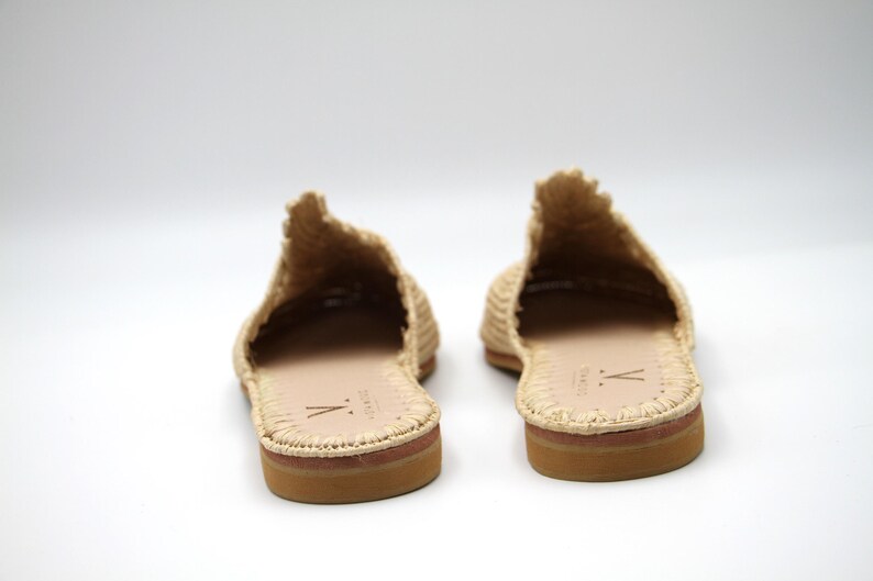 K&ouml;nnte beinhalten: Ein Paar beigefarbene, geflochtene Strohsandalen mit Ledersohle. Die Sandalen haben ein schlichtes Design mit einem geflochtenen Obermaterial und einer geschlossenen Zehenpartie.