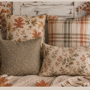 May include: A collection of four decorative throw pillows featuring various patterns. One pillow has an autumn leaf and acorn print, one has a plaid design in orange and green, one is solid olive green with a small pattern, and one has a floral print.