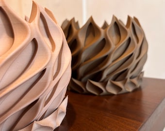 May include: Two decorative, textured vases. One is a light brown color, and the other is a darker brown. The vases have a unique, wave-like design with pointed edges. They are placed on a dark wooden surface.