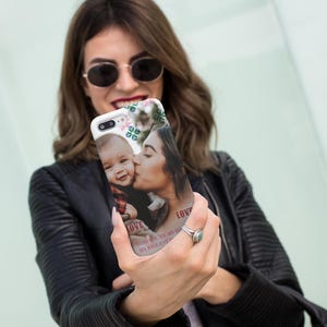 May include: White phone case featuring a photo of a mother kissing a baby. The case has floral accents and the word "LOVE" printed on it. The text "YOU'RE MY HEART, MY BIGGEST BLESSING" is also visible.