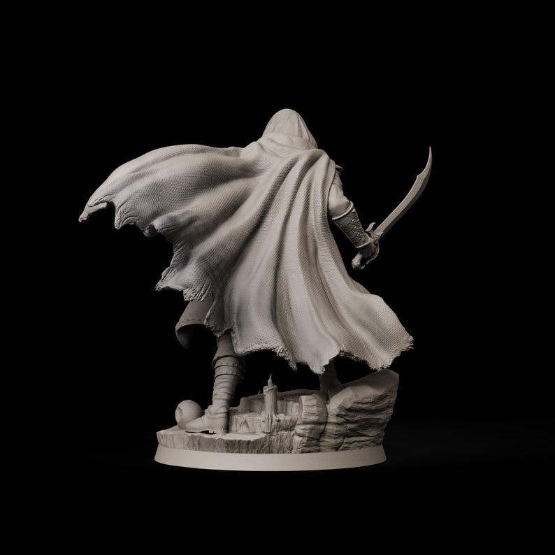 May include: A detailed figurine of a cloaked figure holding a curved sword, standing atop a rocky base with a small castle. The figure is wearing a hooded cloak that drapes dramatically. The statue is a neutral color, set against a black background.