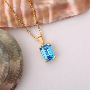 May include: A gold chain necklace with a blue gemstone pendant. The pendant is a rectangular emerald cut.