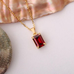 May include: A gold chain necklace with a red gemstone pendant. The pendant is a rectangular shape with a square cut gemstone.