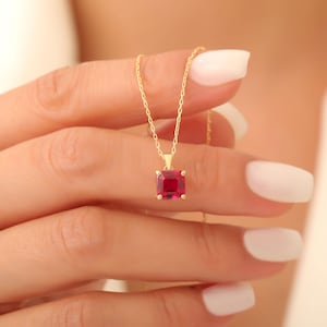 Könnte beinhalten: Eine goldene Kettenkette mit einem quadratischen Anhänger mit einem roten Edelstein.