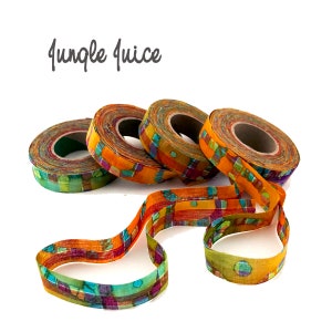 May include: Four spools of colorful fabric ribbon with a geometric pattern in shades of orange, green, purple, and blue. The ribbon is unraveled and lying on a white background. The text "Jungle Juice" is written above the ribbon.