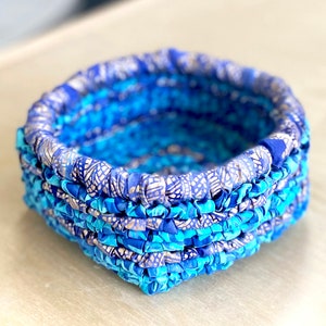 Könnte beinhalten: Ein quadratischer Korb aus blauem und silbernem Stoff. Der Korb ist aus gewebtem Stoff gefertigt und hat ein dekoratives Muster.