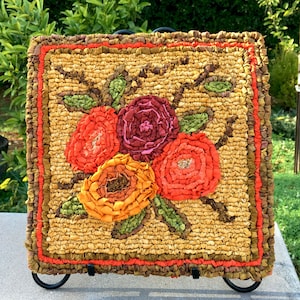 May include: A hand-hooked rug with a floral design featuring three large, colorful flowers in shades of red, orange, and pink. The rug is set against a green background and has a brown border.