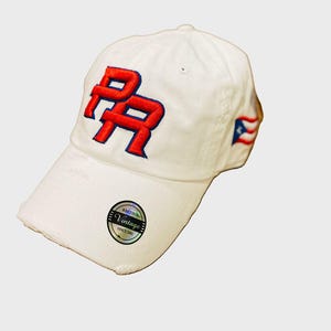 May include: White baseball cap with a red and blue "PR" logo embroidered on the front. The cap has a distressed look and a small, silver "Vintage" label on the side.