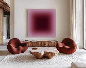 Op de afbeelding: Een vierkant wandkunstwerk met een verloop van lichtroze naar een diep donkerbordeauxrood centrum, geplaatst boven een lange houten consoletafel, twee afgeronde roestkleurige fauteuils en een lage salontafel van hout met organische vormen.