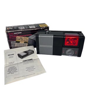 Könnte beinhalten: Ein schwarz-silberner Sears Craftsman Notfall-Auto-Luftkompressor mit roter Taschenlampenlinse. Das Set enthält die Originalverpackung mit aufgedrucktem Text und eine weiße Bedienungsanleitung mit der Modellnummer 9 15041.