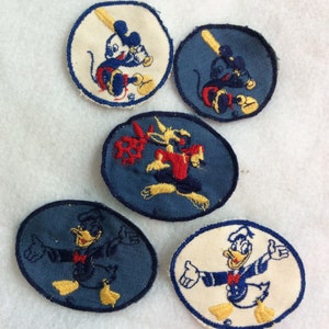 May include: Five vintage embroidered patches featuring Disney characters. Mickey Mouse is shown playing baseball on two patches, one with a white background and the other with a blue background. Donald Duck is shown in a sailor outfit on two patches, one with a white background and the other with a blue background.  Goofy is shown playing basketball on a blue background patch.