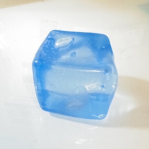 Op de afbeelding: Een doorschijnend, lichtblauw, onregelmatig gevormd object. Het object heeft een licht getextureerd oppervlak en lijkt te zijn gemaakt van een vast materiaal. De vorm doet denken aan een kleine, abstracte sculptuur of een decoratief stuk.