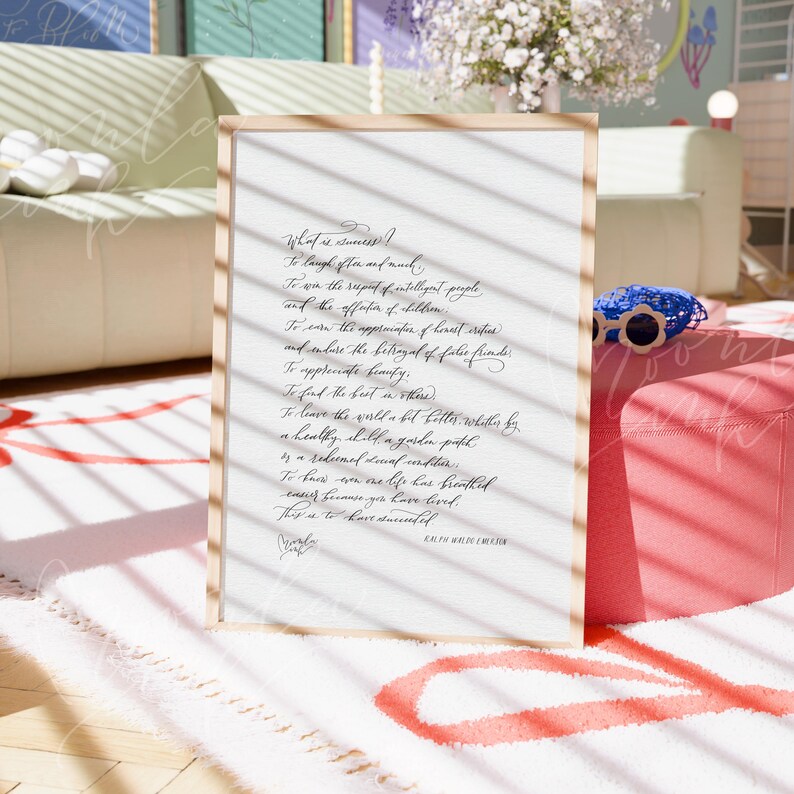 May include: A framed print with a light wood frame. The print features elegant cursive text on a white background. The text reads "What is success?" followed by a poem. A blue and white accessory sits nearby.