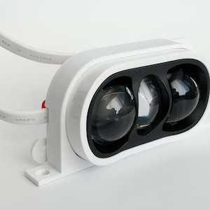 May include: A white electronic device with three dark, spherical lenses set in a black frame. The device has a white, rectangular housing and a white cable attached. The overall design is modern and sleek.