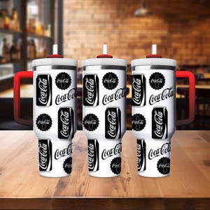 May include: Three white insulated tumblers with red handles and lids. Each tumbler is decorated with a repeating pattern of black Coca-Cola cans and logos. The tumblers are on a wooden surface.