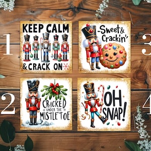 May include: Four square Christmas art prints with nutcracker illustrations and festive text. The prints display phrases such as "Keep Calm & Crack On" and "Oh Snap!" against a wooden backdrop.