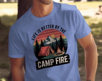 Könnte beinhalten: Blaues T-Shirt mit Camping-Grafik. Das Design zeigt ein rotes Zelt, ein Lagerfeuer, Berge und Bäume unter einem Sonnenuntergang. Der Text lautet "LIFE IS BETTER BY THE CAMP FIRE."