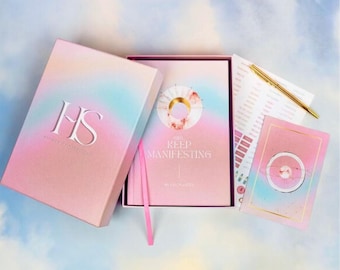 Può includere: Una scatola ombré rosa e blu con il testo "HS" e "Highly Sensitive" sul davanti. La scatola contiene un diario ombré rosa e blu con il testo "You Keep Manifesting" e una penna rosa.