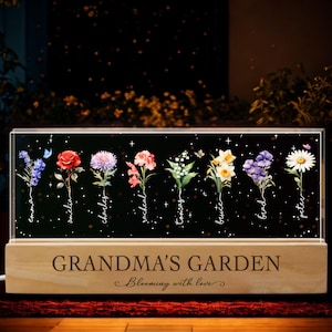 May include: A wooden light-up box with a black background and a white inscription that reads "Grandma's Garden, Blooming with Love". The box features a row of eight watercolor flowers with names written below each flower.