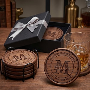 May include: A set of round wooden coasters with a dark brown finish, featuring a laser-engraved letter M, the name MILLER, and the text PREMIUM RESERVE BATCH EST. 2026 KENTUCKY. The coasters are stored in a black metal holder and a gift box.