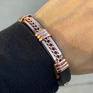 May include: A black leather bracelet with a rose gold chain and accents. The bracelet has a simple design and is a stylish accessory.