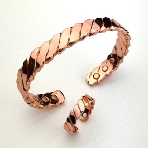 May include: A copper bracelet and ring with a braided design and magnetic closures. The bracelet is open and the ring is closed.